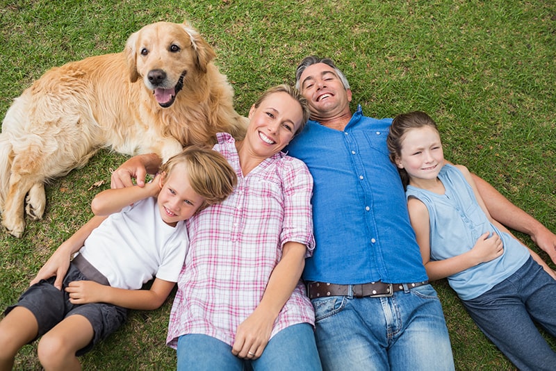 A dog, son, mom, dad, and daughter laying in the grass together smiling