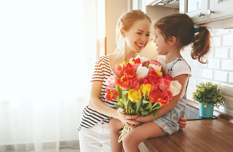 Mom holding daughter sitting on counter with a bounquet of flowers in their hands